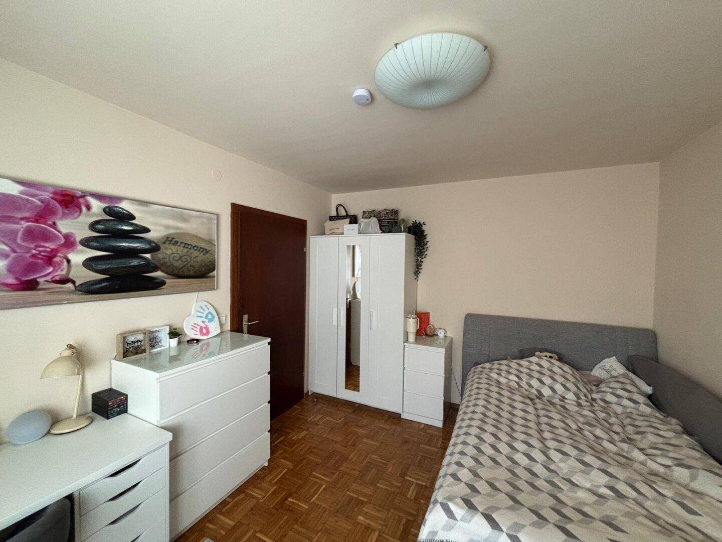Gemütliches Schlafzimmer mit Holzboden, weißem Kleiderschrank und dekorativem Wandbild.