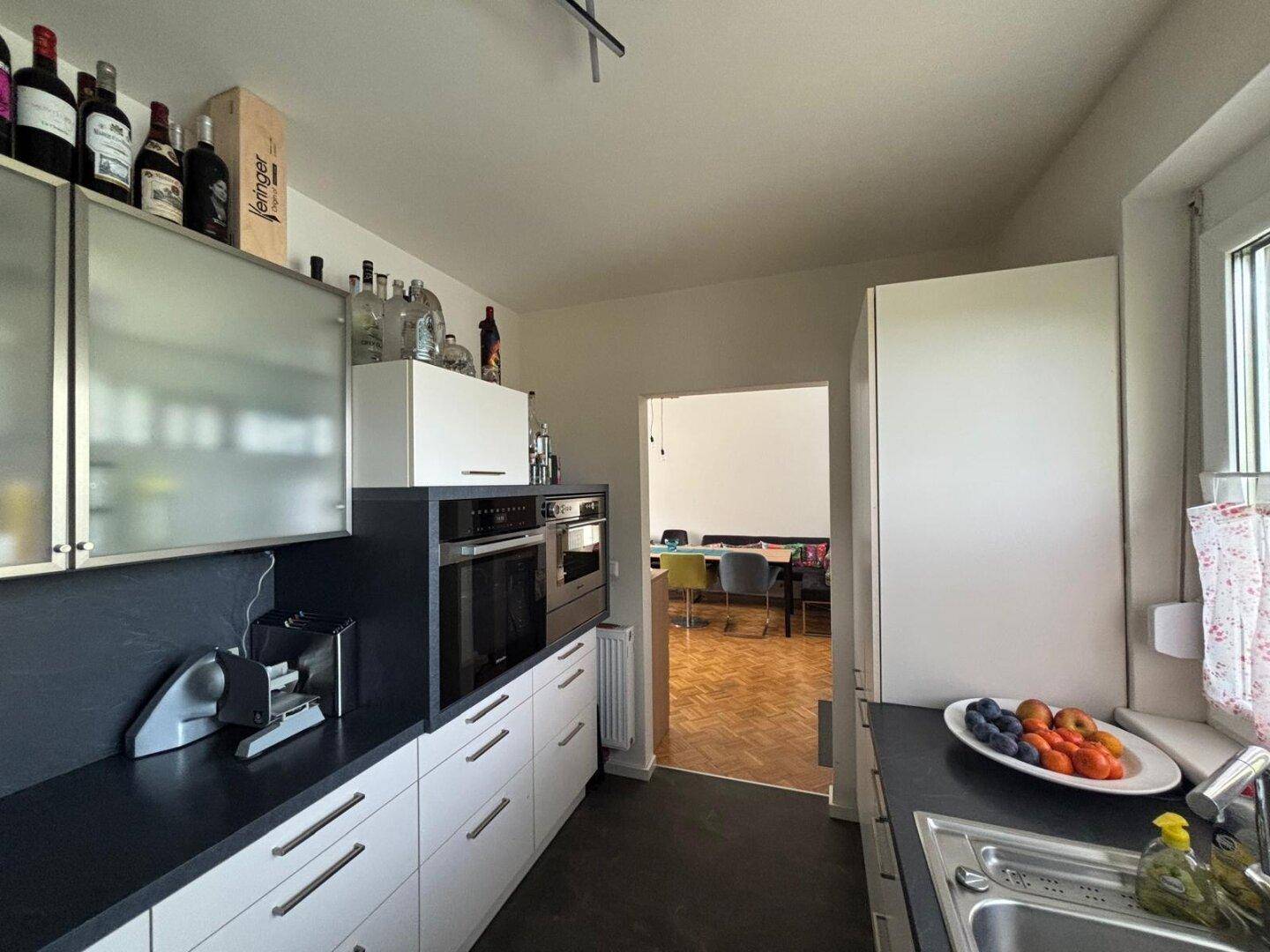 Funktionale Küche mit Fenster, weißen Schränken und Durchgang zum Essbereich.