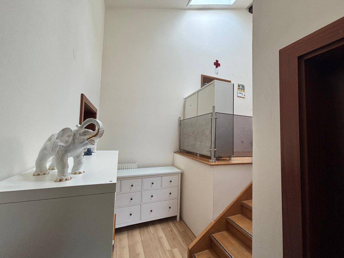 Heller Flurbereich mit Holztreppe, Oberlicht und moderner Glasbrüstung.