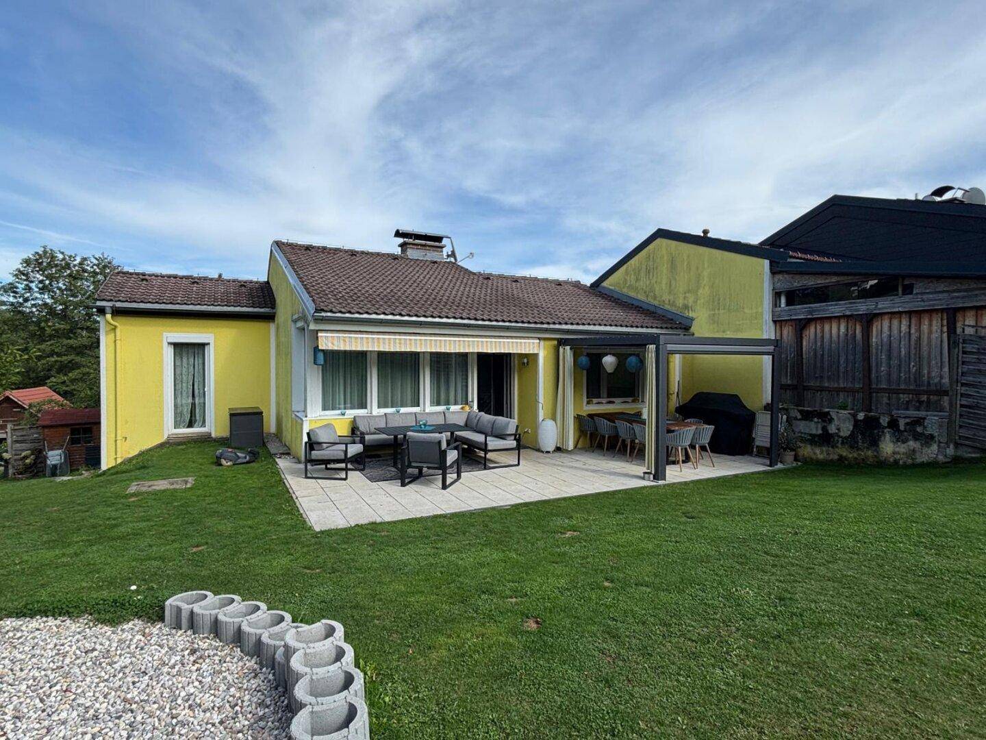 Weitläufiger Garten mit Rasenfläche, Feuerstelle und gepflasterter Terrasse am Haus.