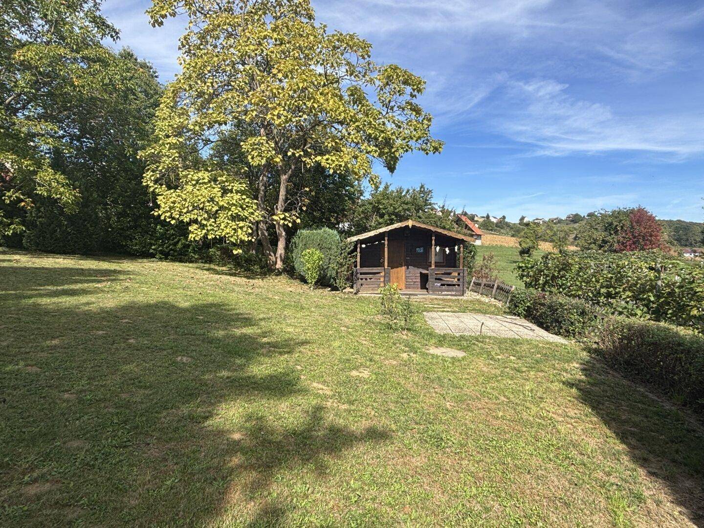 Kleiner Holzschuppen mit überdachter Veranda auf einer sonnigen Rasenfläche im Garten.