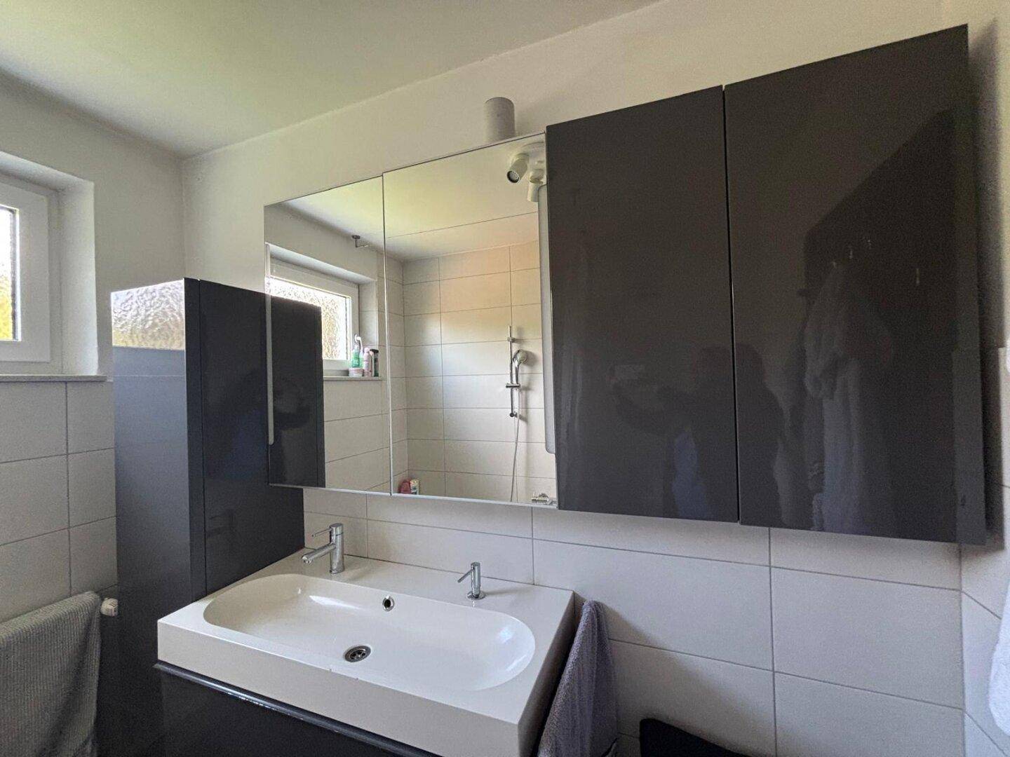 Modernes Badezimmer mit Doppelwaschbecken, Spiegelschrank und dunklen Hängeschränken.