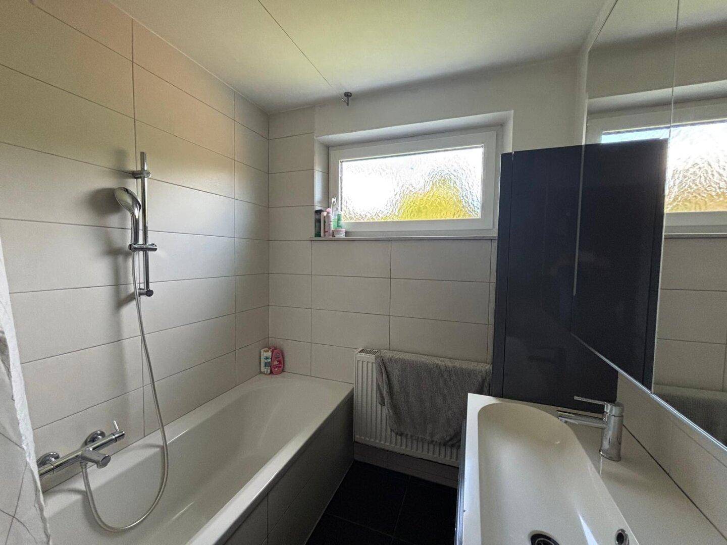 Badezimmer mit Badewanne, Duscharmatur, Waschbecken und Fenster für natürliches Licht.