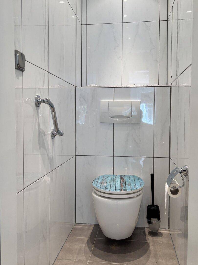 Gäste-WC mit wandhängender Toilette, Haltegriff und modernen Fliesen.