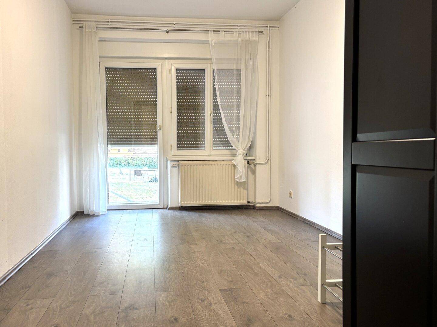 Leeres Schlafzimmer mit Laminatboden und Zugang zu einem Balkon oder Garten.