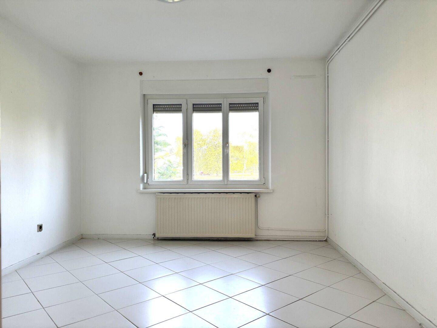Helles Schlafzimmer mit Fliesenboden und großem Fenster mit Rollläden.