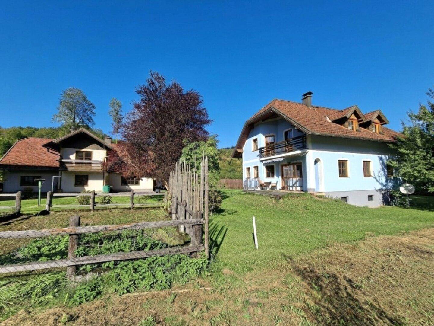 Ländliches Anwesen mit zwei Häusern und grüner Umgebung unter blauem Himmel.