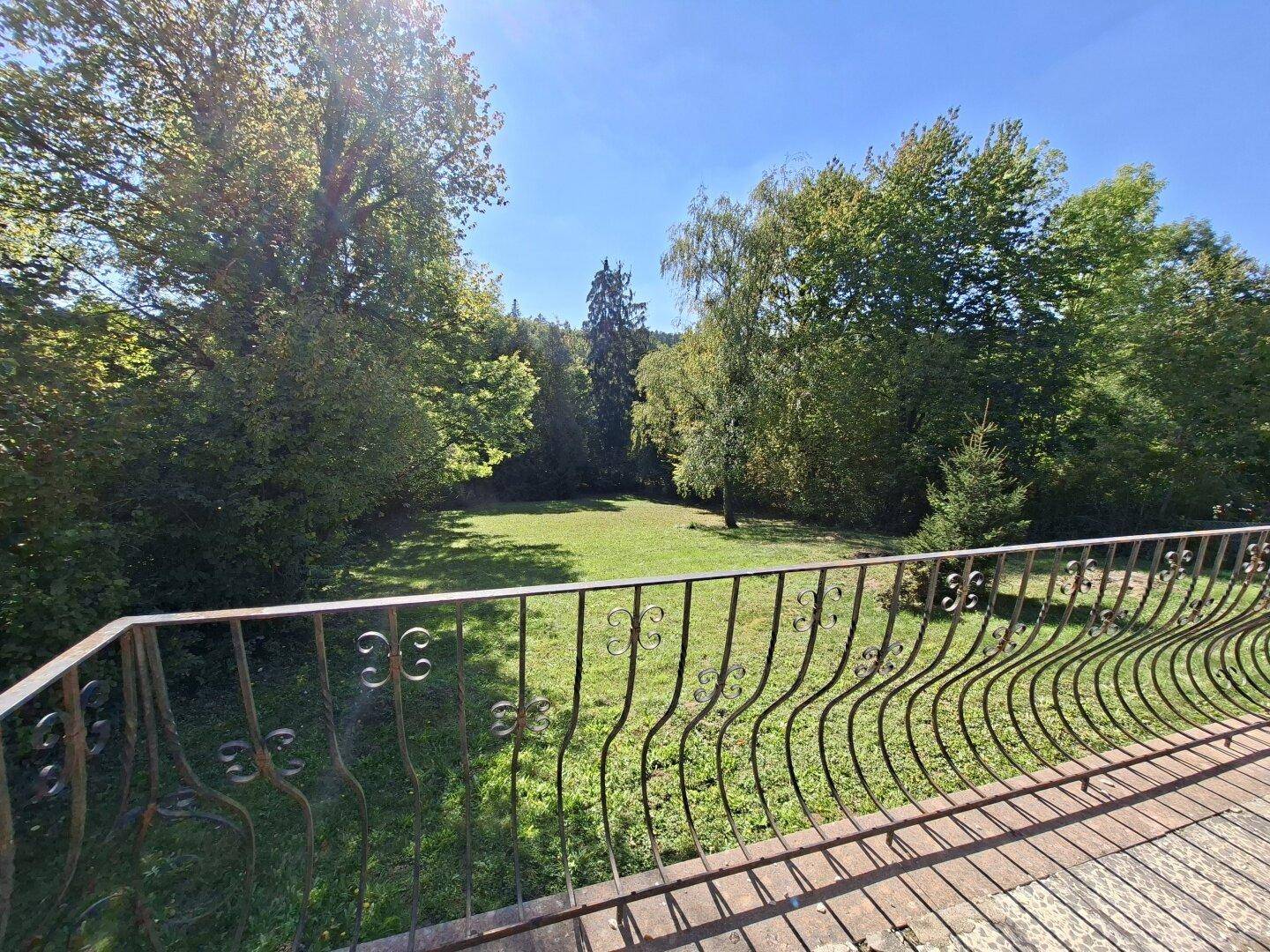 Blick von einem Balkon mit schmiedeeisernem Geländer auf eine weite grüne Rasenfläche und Bäume.