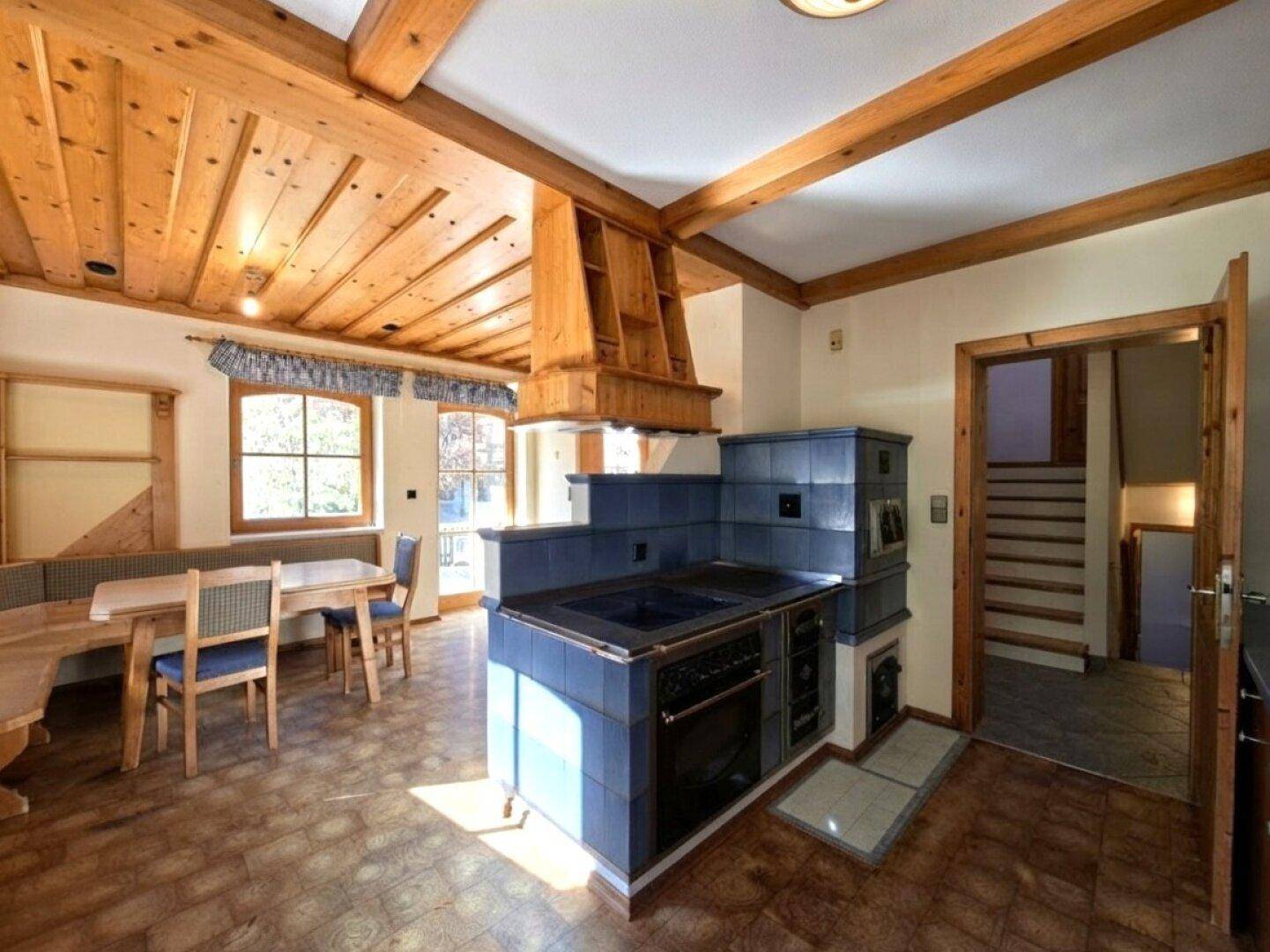 Traditionelle Wohnküche mit Kachelofen, Holzbalkendecke und Essbereich.