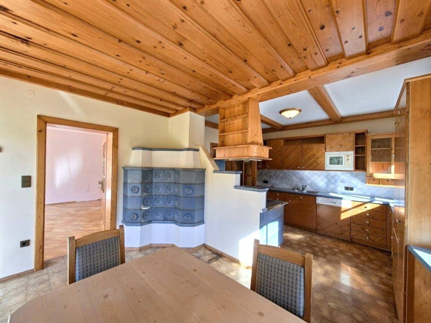 Rustikale Küche mit Kachelofen, Holzeinbauten und Essbereich, offen zum Wohnraum.