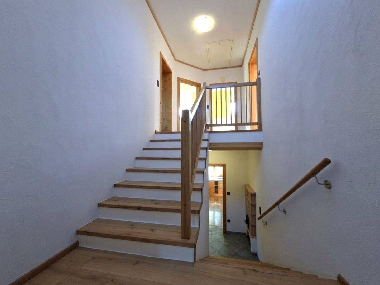Heller Treppenaufgang mit Holzstufen und Geländer, verbindet die Stockwerke.