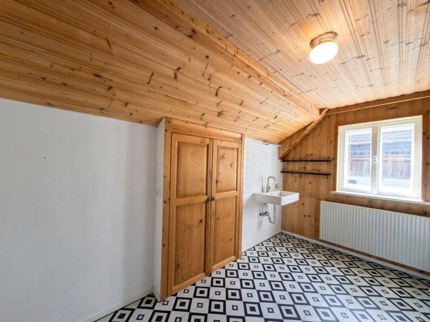Raum mit Holzwänden, schrägen Decken und einem Waschbecken, ideal als Abstellraum.
