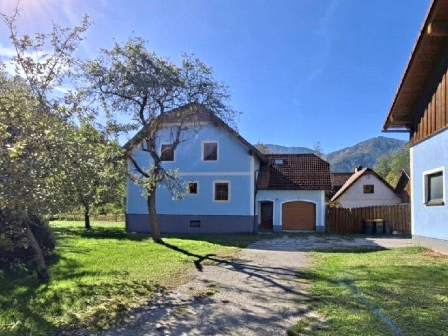 Blau gestrichenes Haus mit rotem Dach und Garage, umgeben von grüner Wiese.