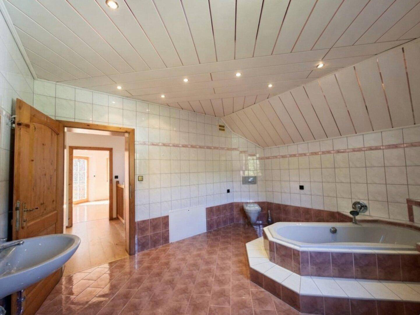 Geräumiges Badezimmer mit Eckbadewanne, Fliesenboden und schräger Decke.