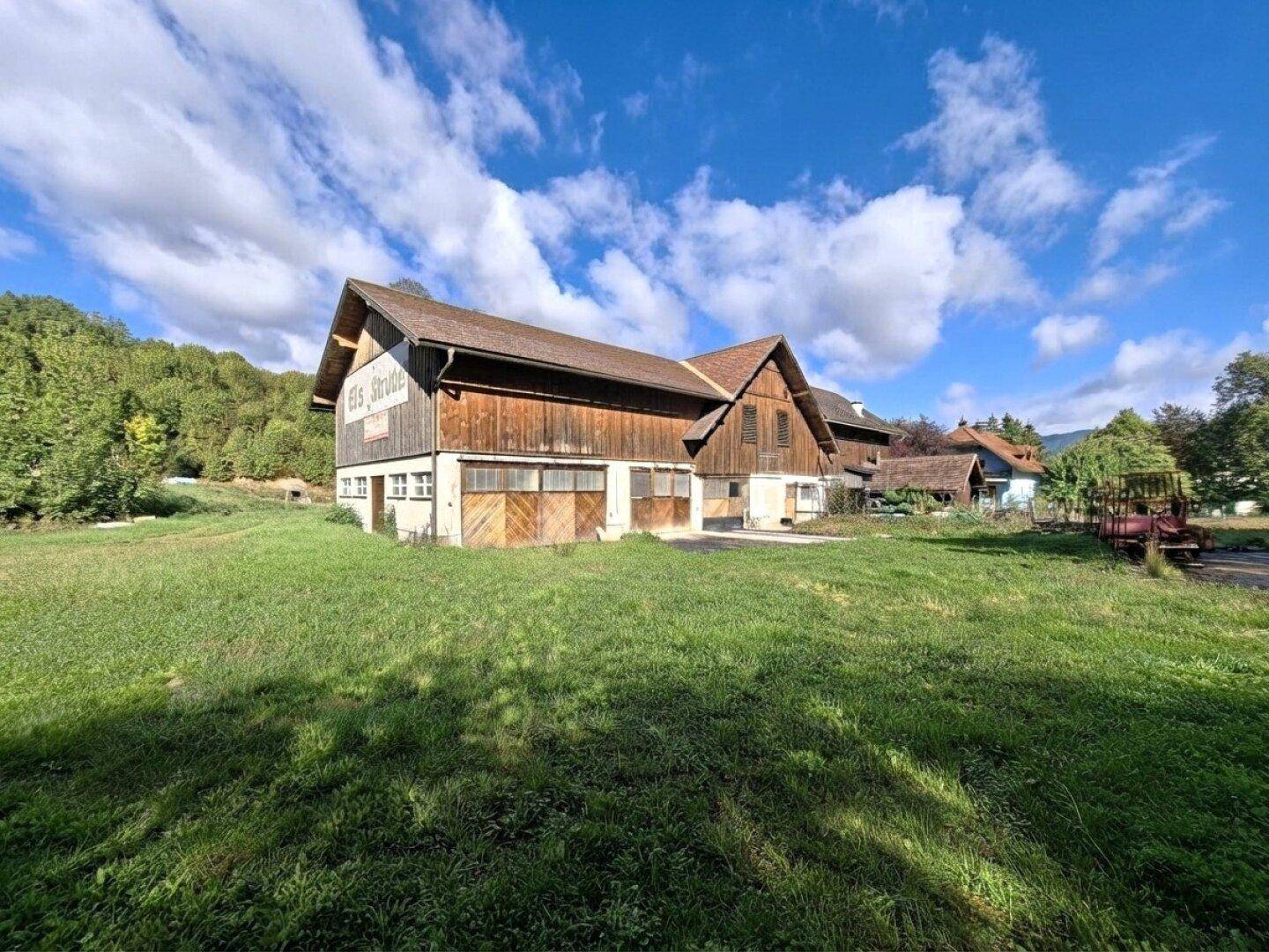 Geräumiges Wirtschaftsgebäude mit Holzwänden und mehreren Toren, umgeben von Wiese.
