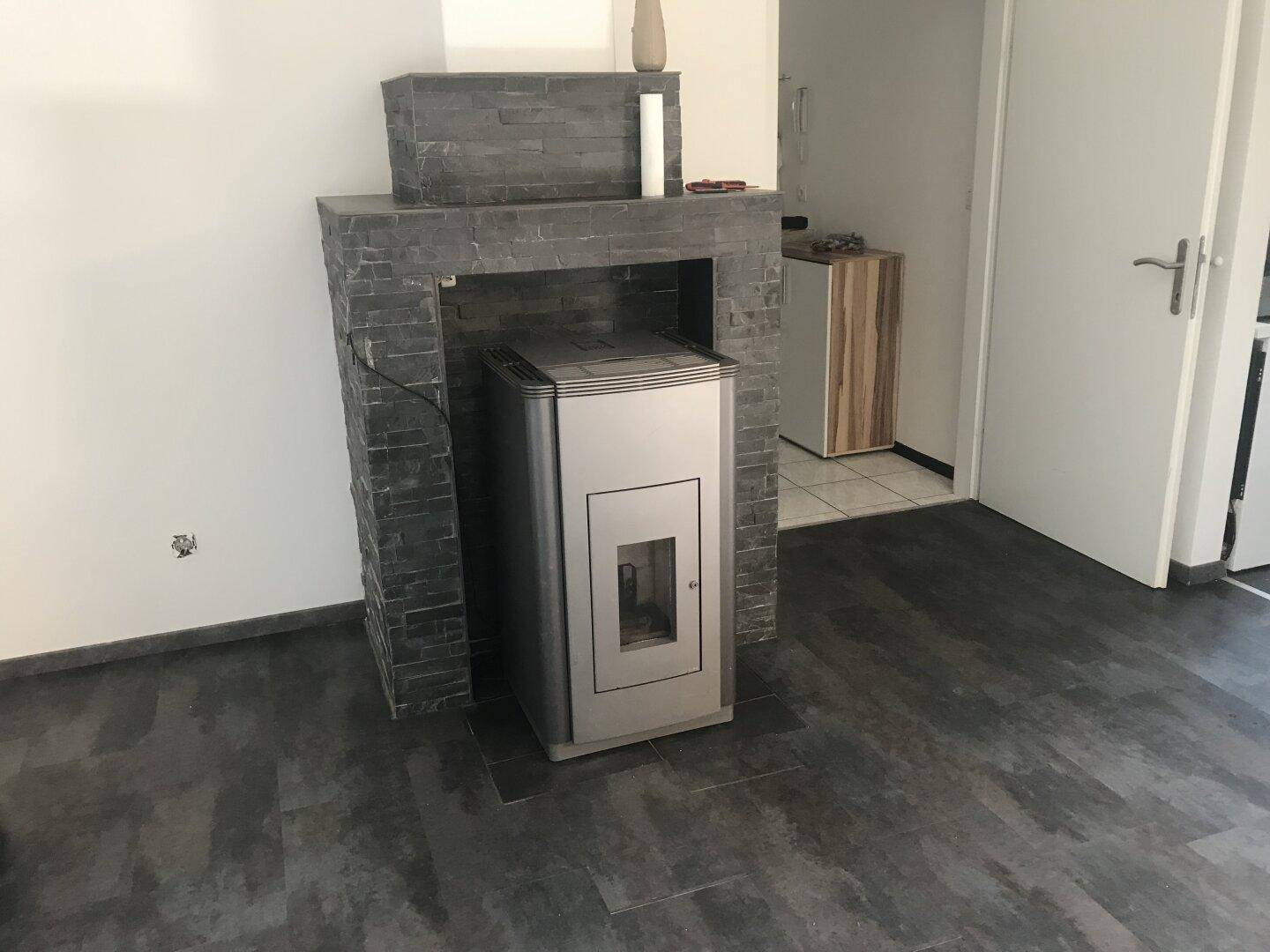 Moderner Pelletofen in einem Wohnbereich mit dunklem Laminatboden und Steinverkleidung an der Wand.