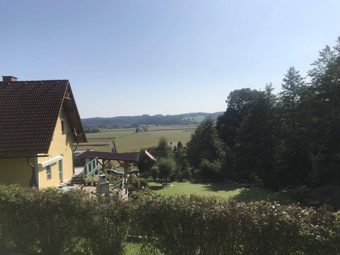 Weitläufiger Garten mit Rasenfläche und Blick auf die umliegende Landschaft und Wälder.