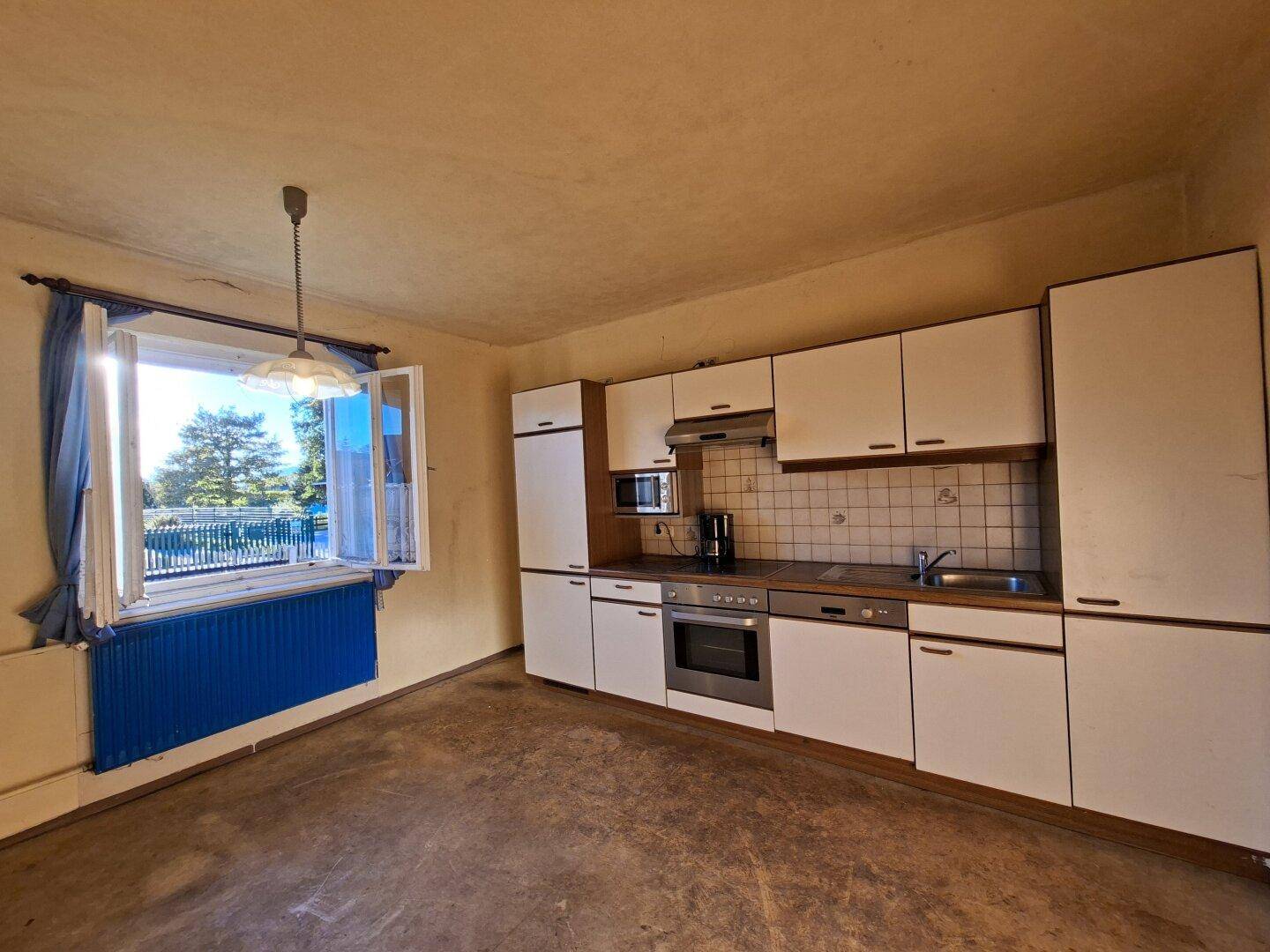Einfache Küche mit weißen Schränken, Einbaugeräten und einem Fenster mit Ausblick.