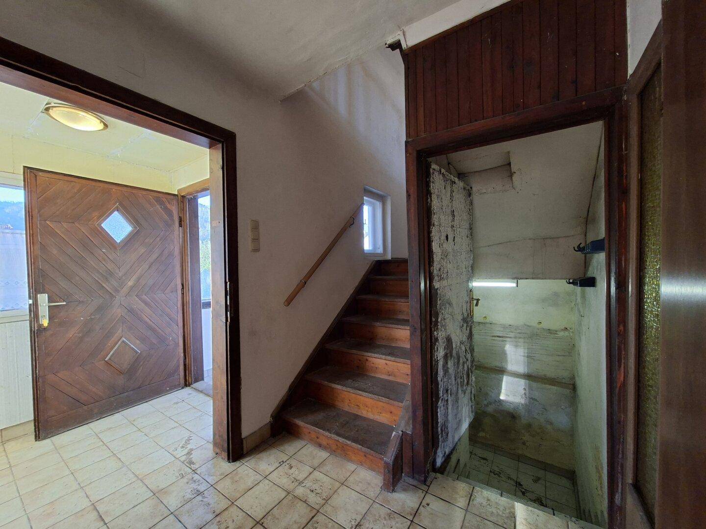 Eingangsbereich mit Holztreppe, gefliestem Boden und Zugang zu einem Kellerraum.