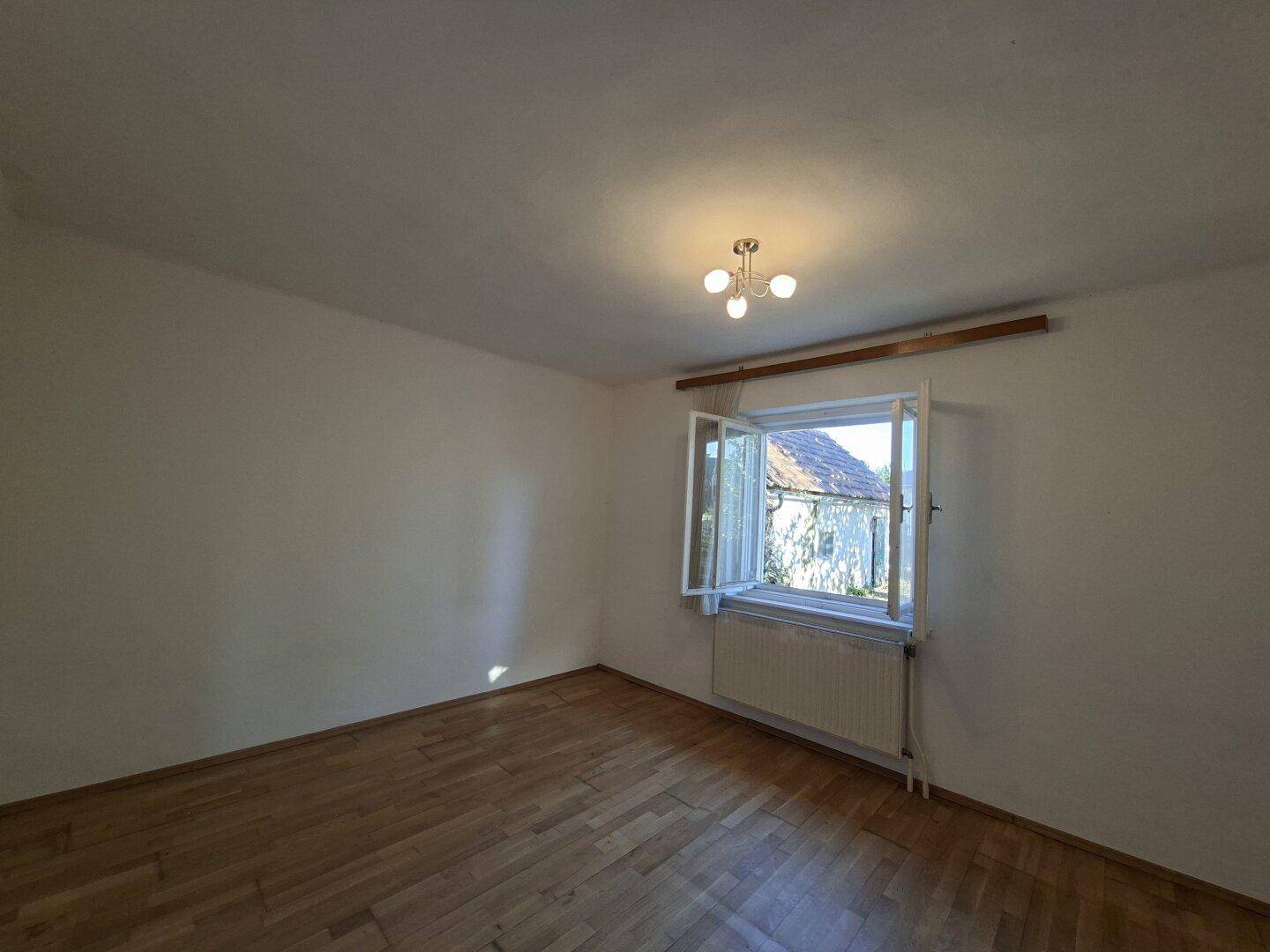 Schlafzimmer mit Holzparkettboden und einem Fenster, das viel Tageslicht hereinlässt.