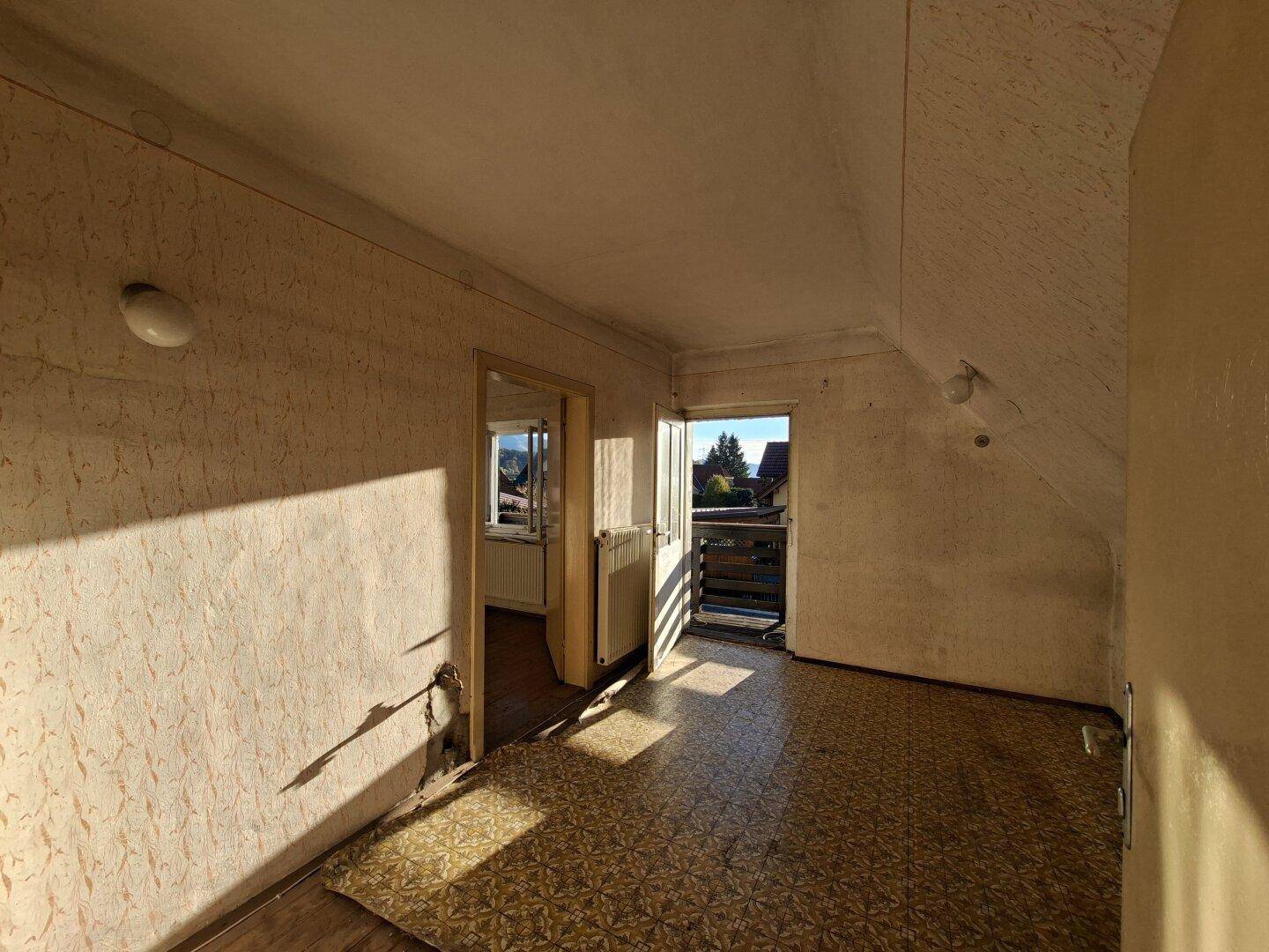 Dachzimmer mit gemusterter Tapete, Zugang zum Balkon und schrägen Wänden.