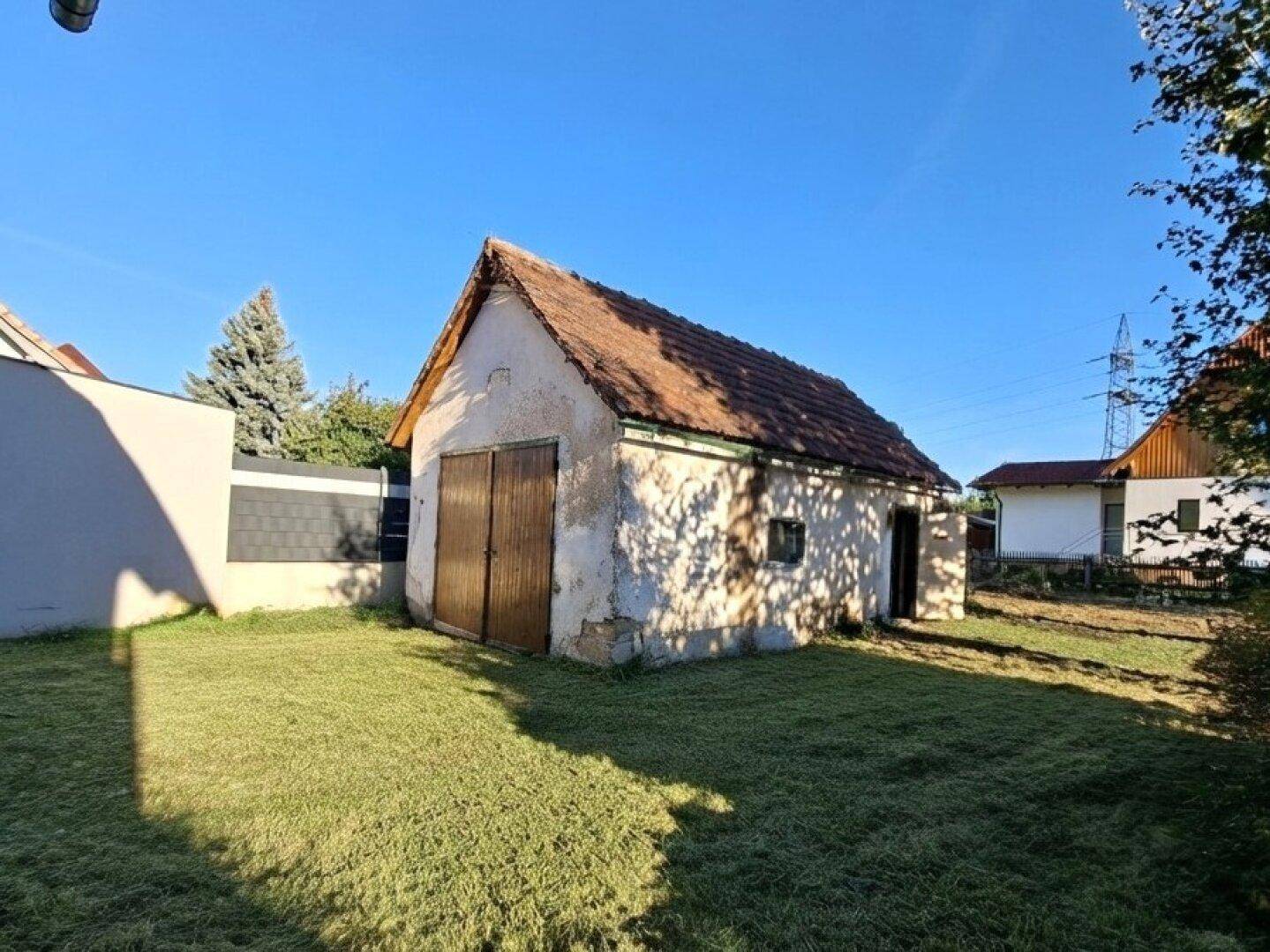 Altes Nebengebäude mit Holztüren und Rasenfläche im Sonnenschein.