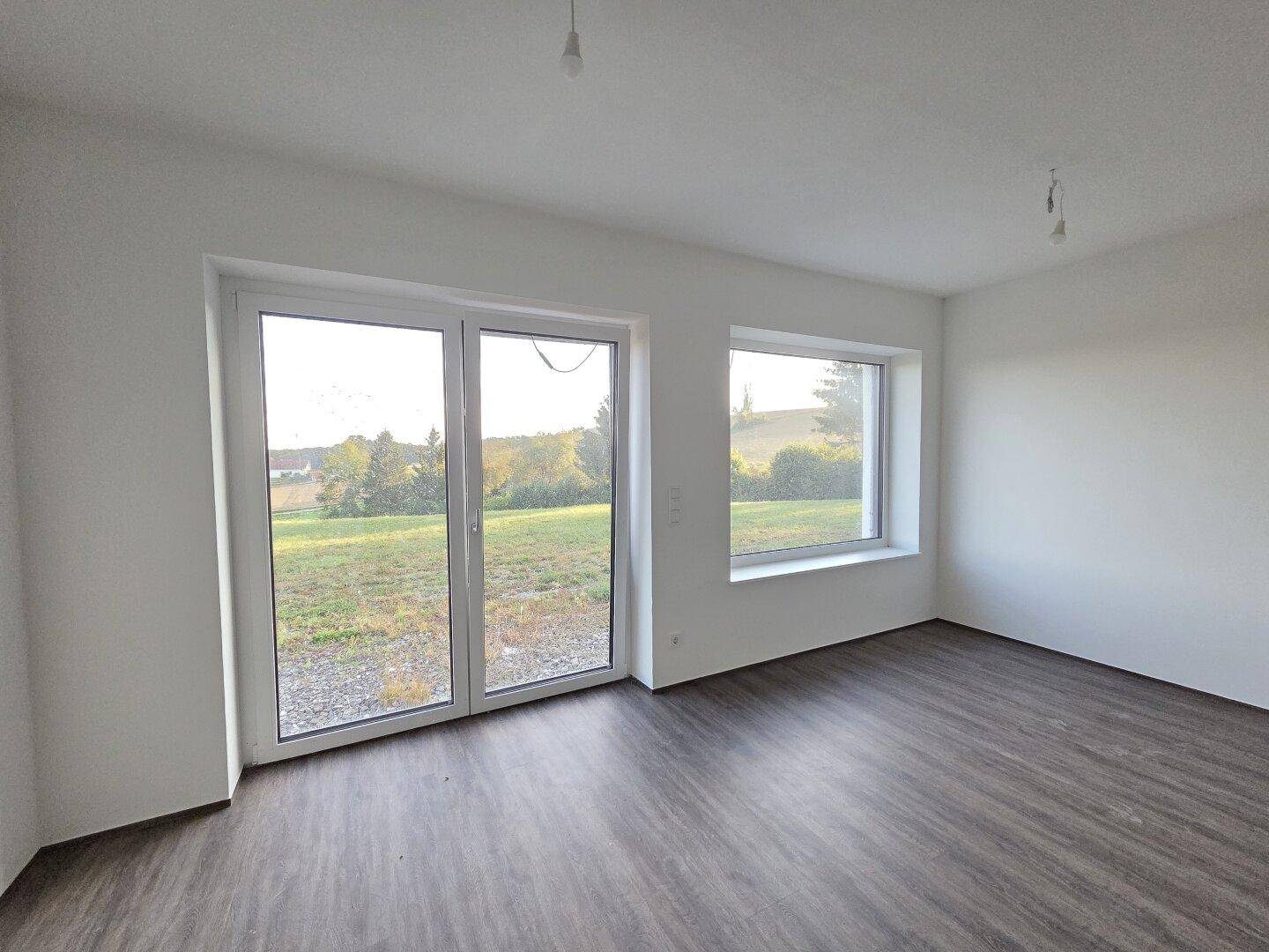 Heller Raum mit großen Fenstern und Zugang zum Garten, ausgestattet mit Laminatboden.