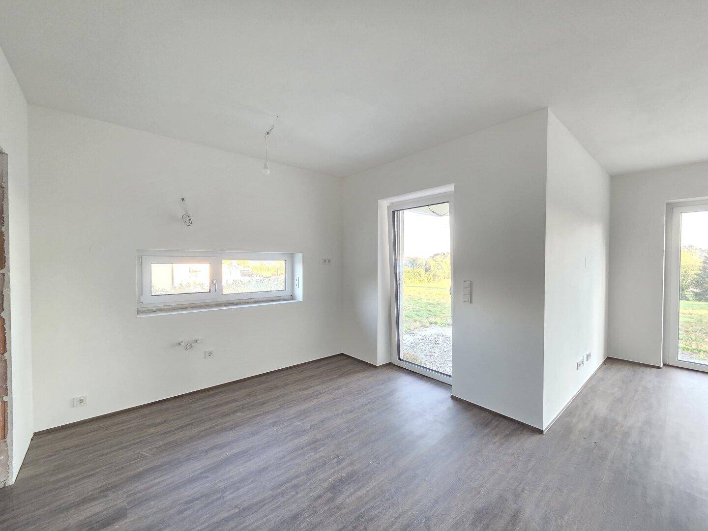 Lichtdurchfluteter Raum mit Laminatboden und Zugang nach draußen, ideal für Wohnzwecke.