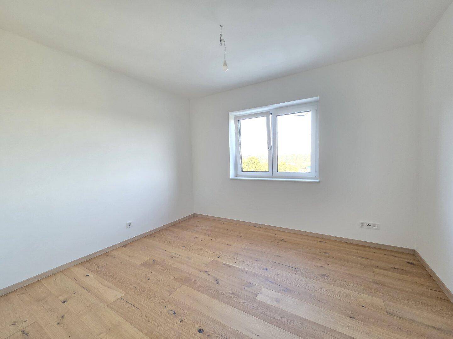 Helles Schlafzimmer mit neuem Parkettboden und einem großen Fenster mit Blick ins Grüne.