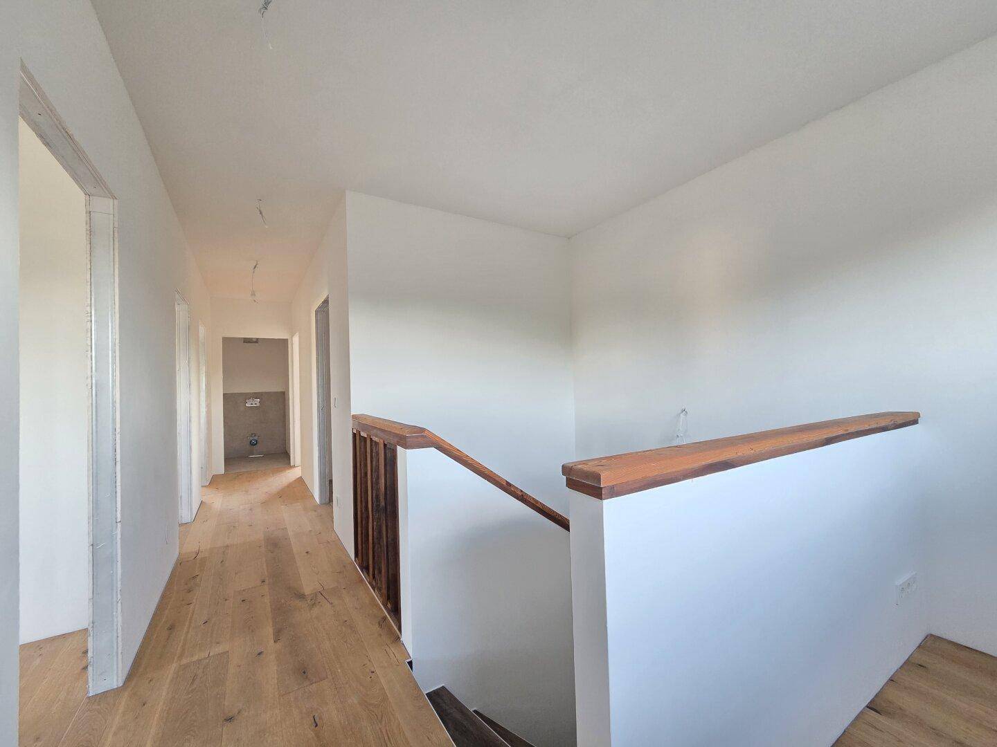 Langer Flur mit Holzparkett und Treppenaufgang, der verschiedene Räume im Haus verbindet.