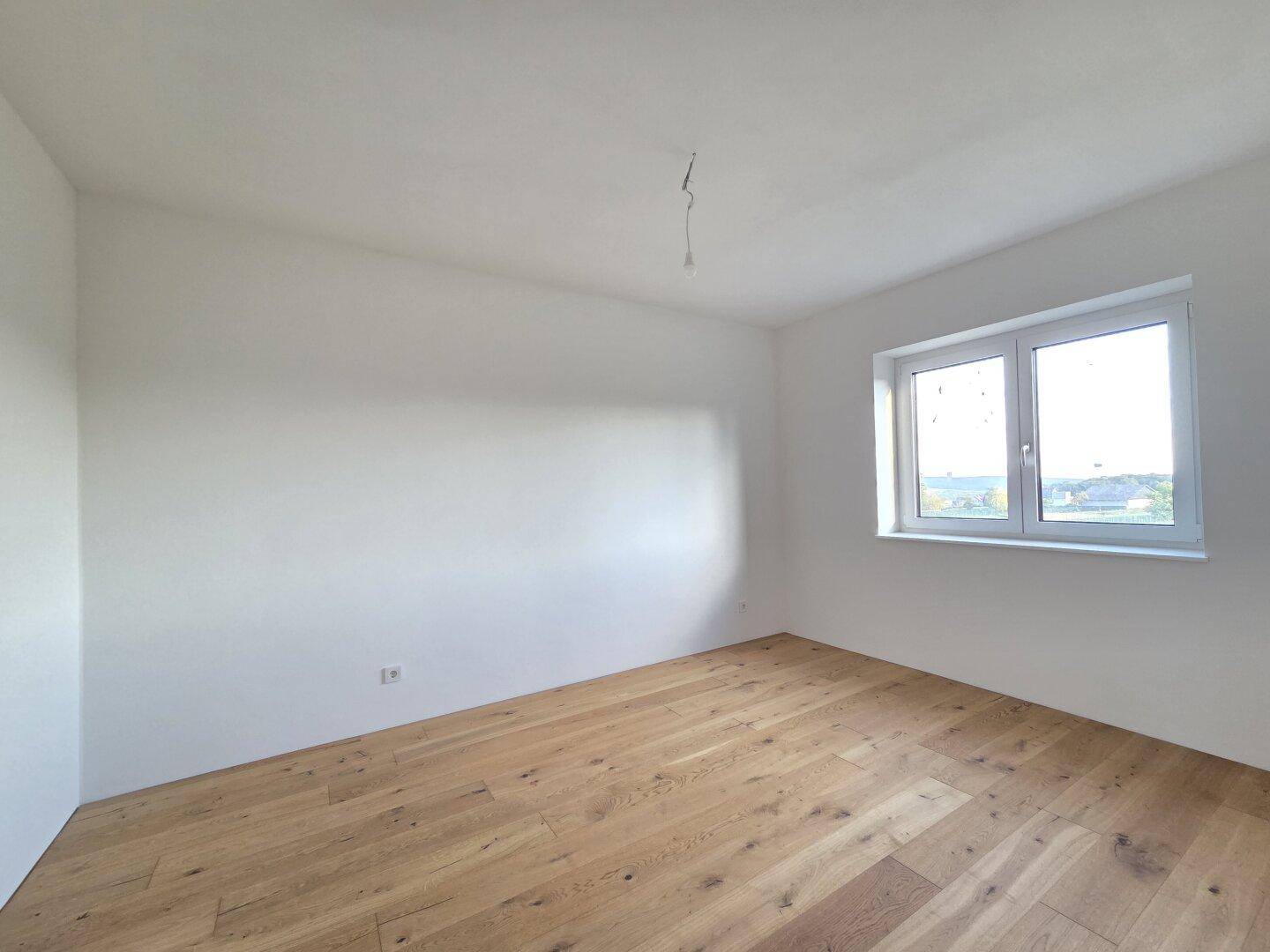 Geräumiges Schlafzimmer mit hellem Parkettboden und einem Fenster, das viel Tageslicht hereinlässt.