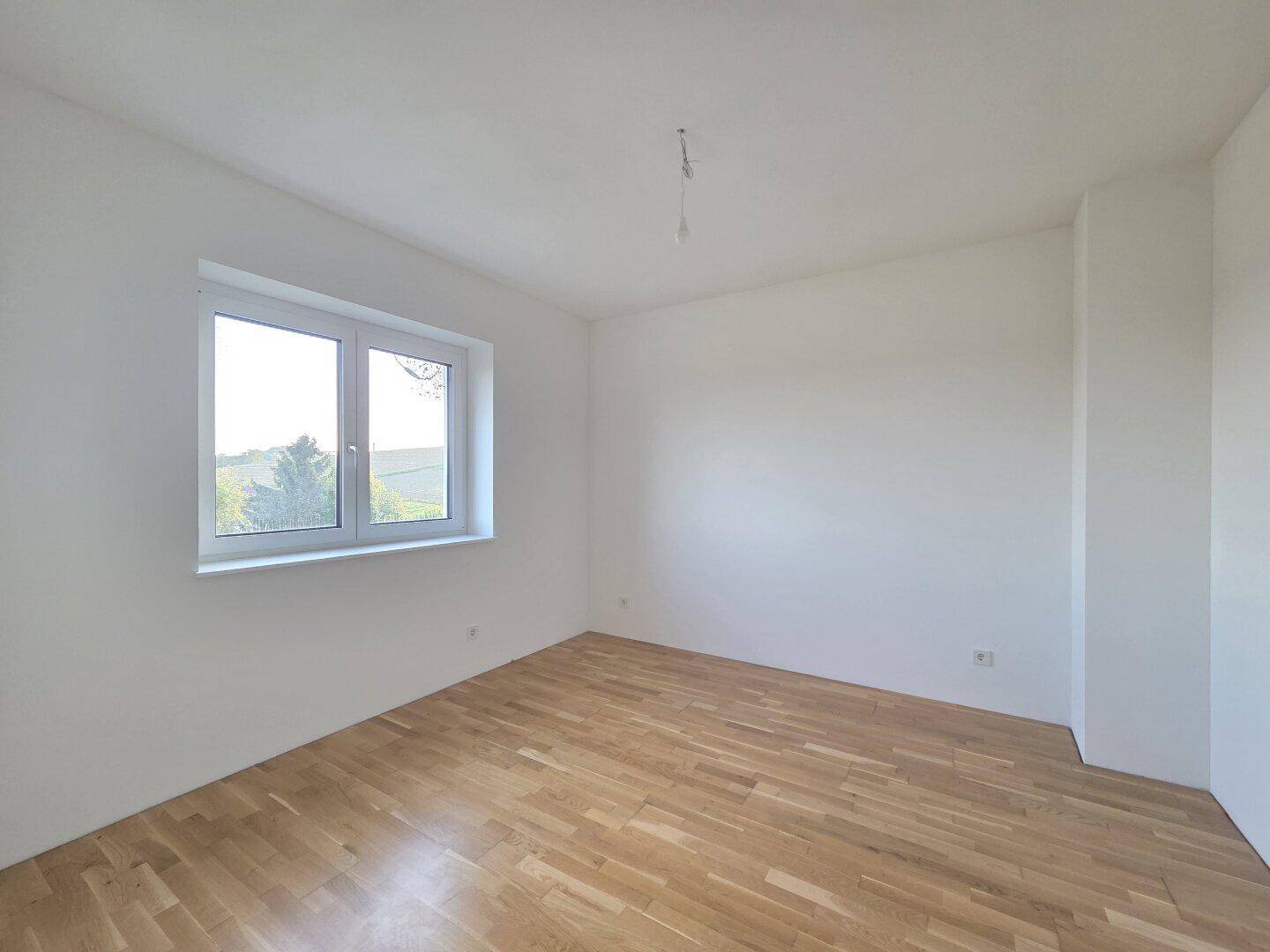 Helles Schlafzimmer mit Parkettboden und einem Fenster, das einen weiten Blick bietet.