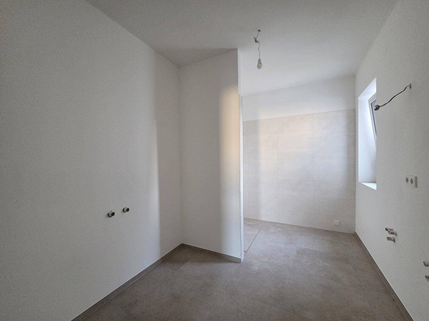 Unfertiges Badezimmer mit grauen Bodenfliesen und Wandanschlüssen, bereit für die Installation.