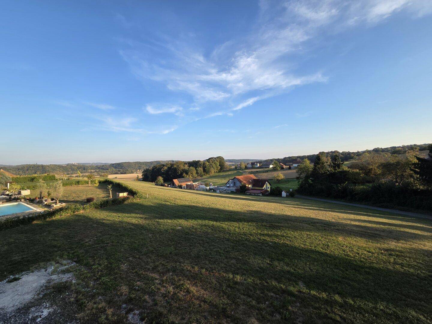 Weitläufige Landschaft mit grünen Feldern und Wäldern unter blauem Himmel, inklusive Poolbereich.