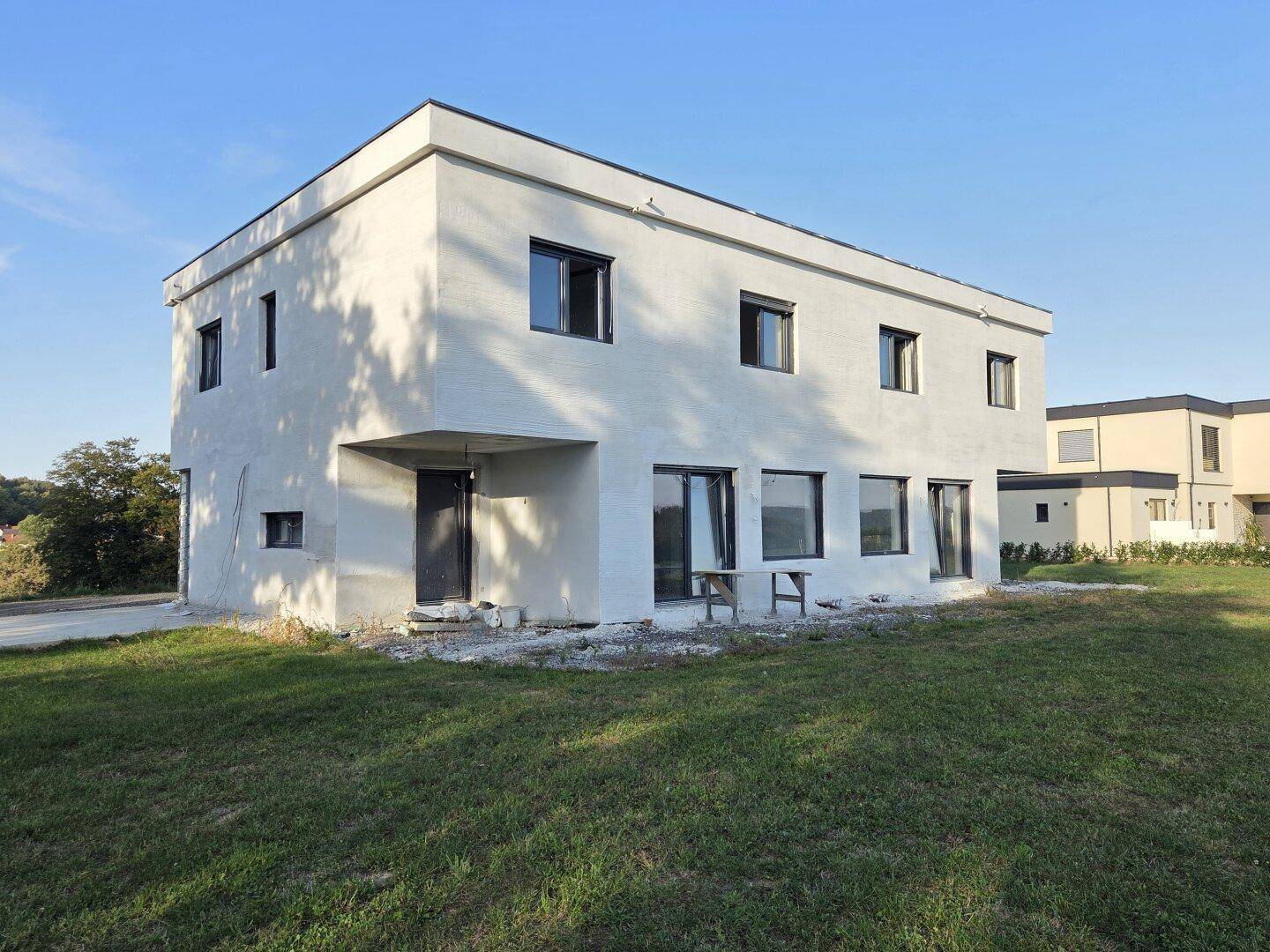 Rückansicht eines modernen Neubauhauses mit großen Fenstern und angrenzender Rasenfläche.