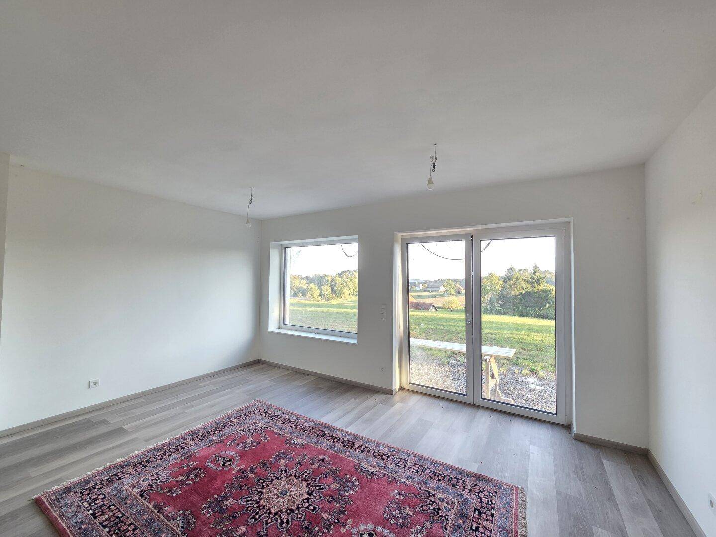 Geräumiges Wohnzimmer mit Laminatboden, großem Fenster und Zugang zum Außenbereich.