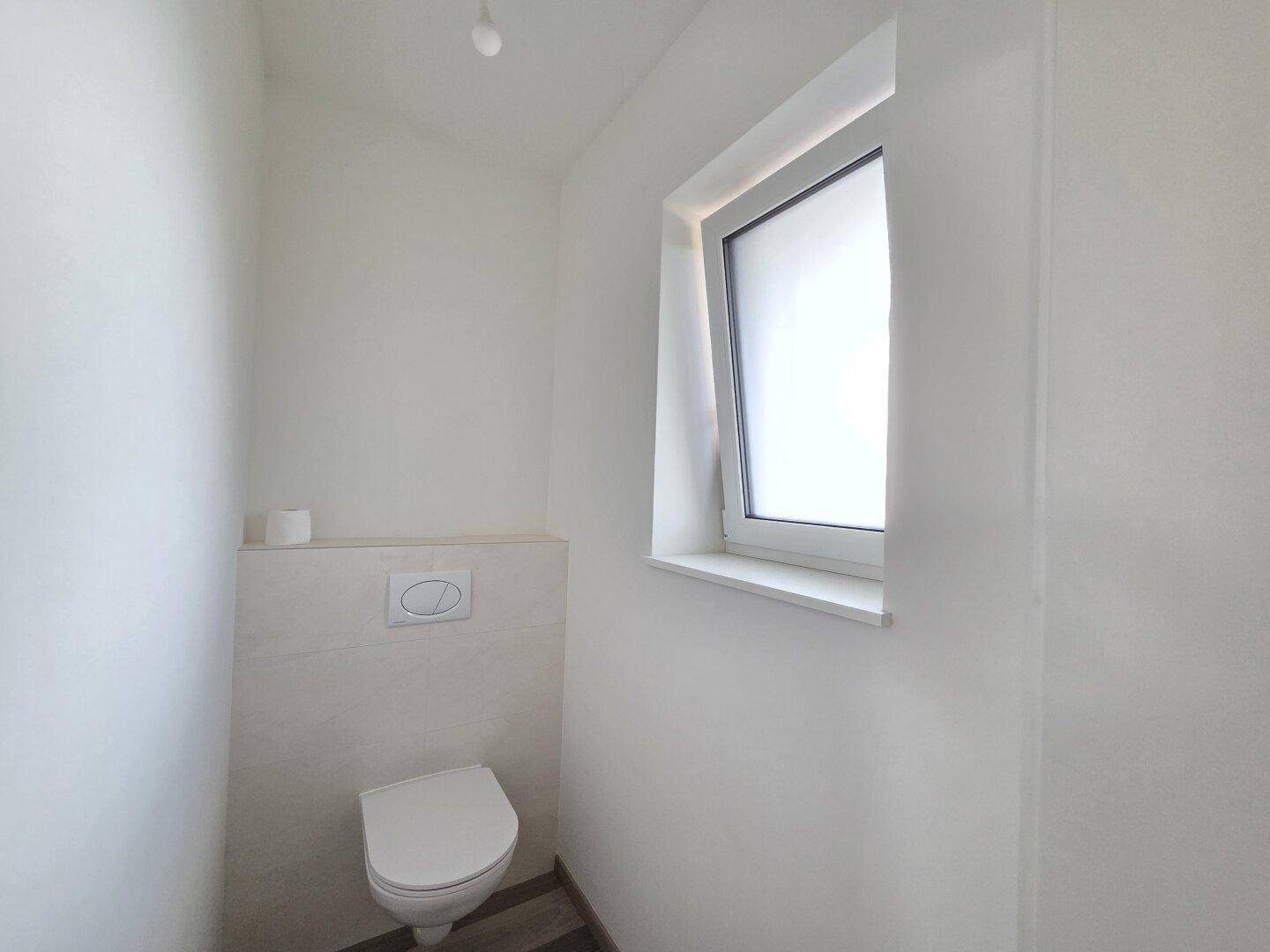 Modernes Gäste-WC mit wandhängender Toilette, Fliesen und einem Fenster für Tageslicht.