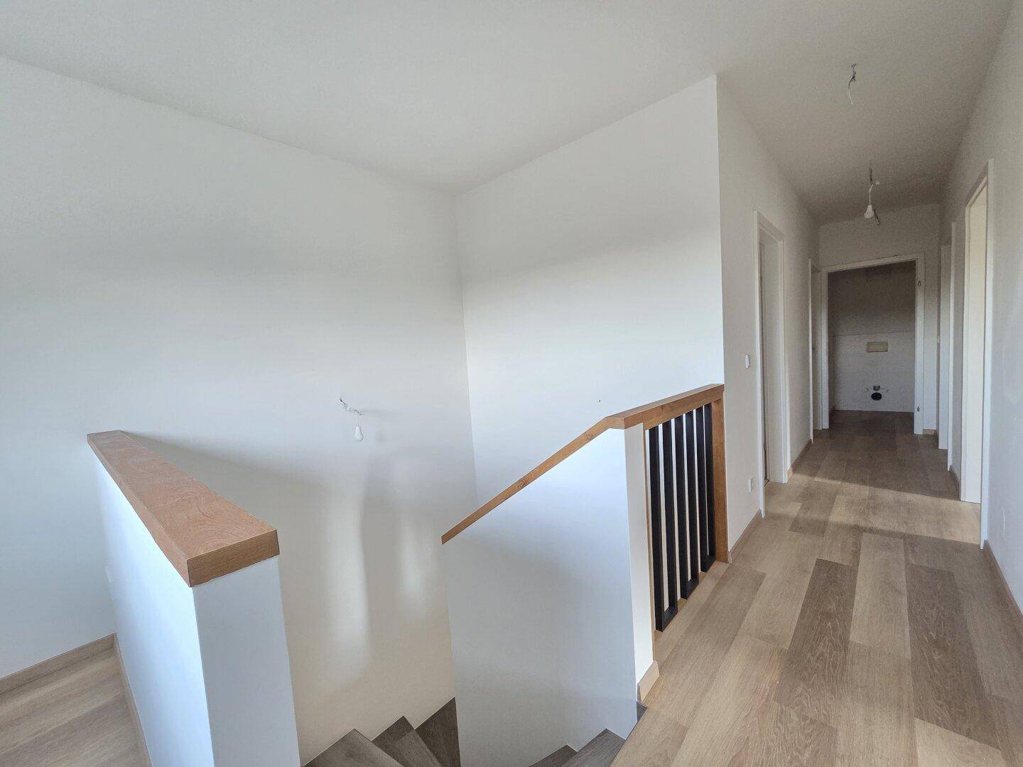 Heller Flur mit Holztreppe und modernem Geländer, der zu weiteren Räumen führt.