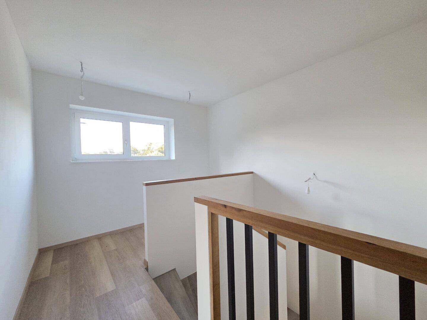 Heller Treppenabsatz im Obergeschoss mit Laminatboden und einem Fenster.