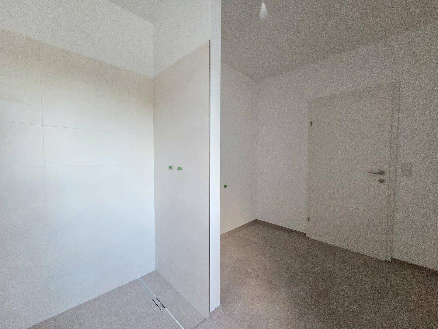Unfertiges Badezimmer mit Duschbereich und gefliesten Wänden, bereit für den Ausbau.