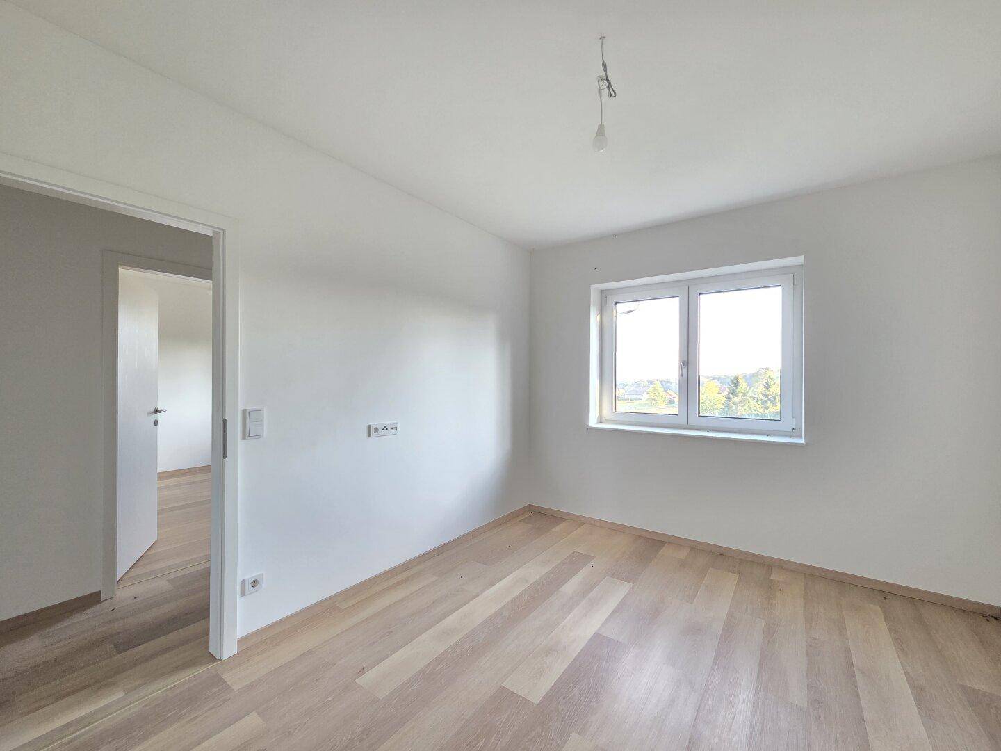 Helles Schlafzimmer mit Laminatboden und einem Fenster, das einen Blick ins Grüne bietet.