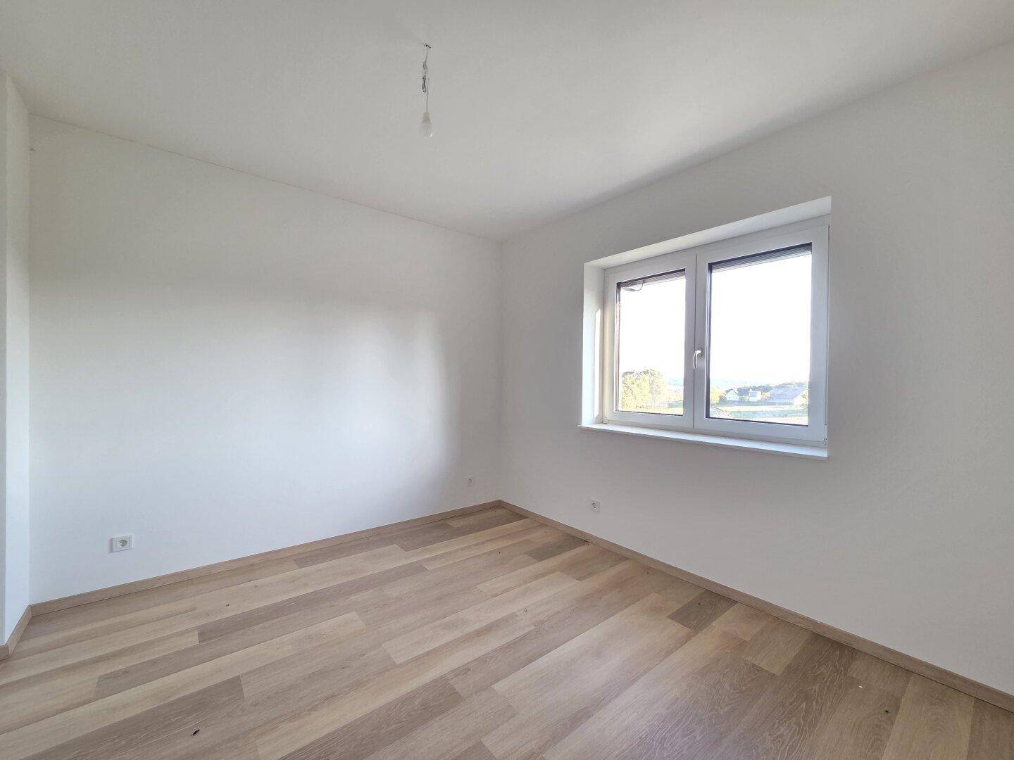 Unmöbliertes Schlafzimmer mit Laminatboden und einem Fenster, das für gute Belichtung sorgt.