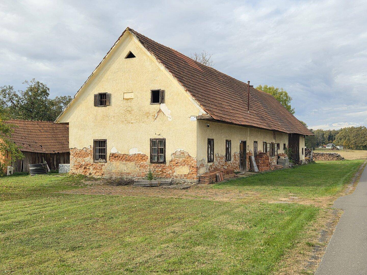 Fassade eines älteren Landhauses mit Putzschäden und traditionellem Ziegeldach in ländlicher Umgebung.