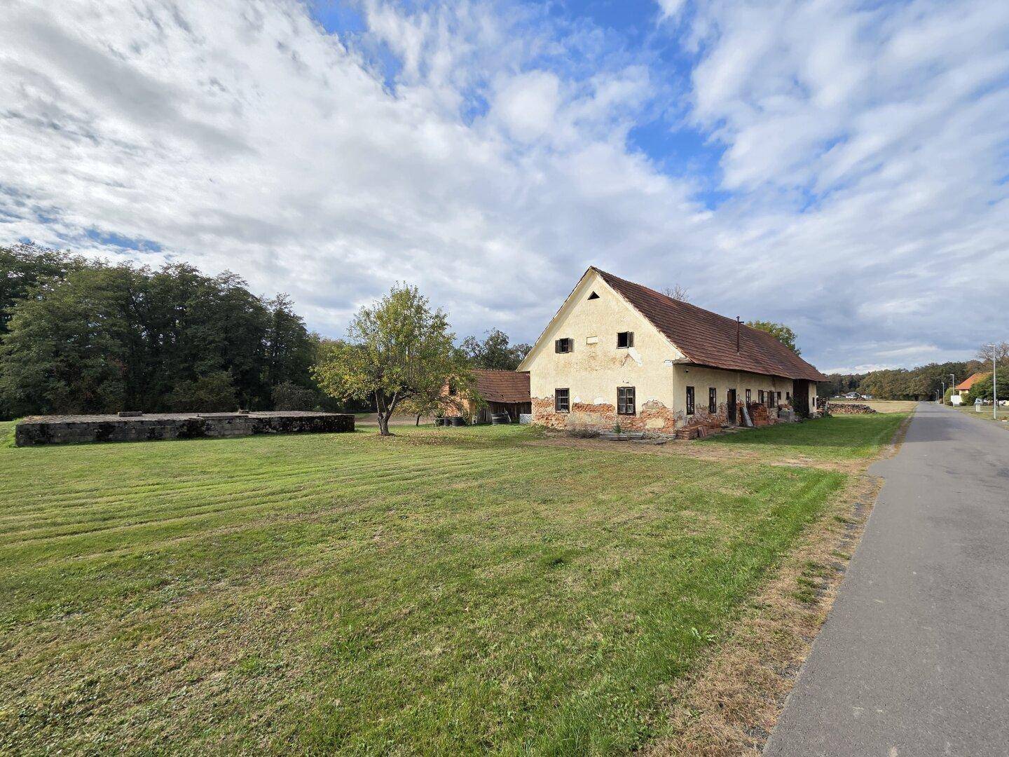 Weitläufiges Grundstück mit einem alten Landhaus und einem Betongebäude unter weitem Himmel.