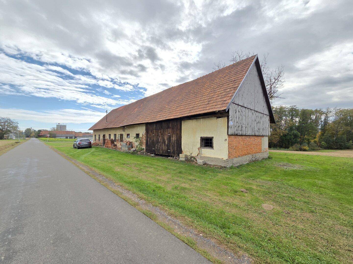Seitenansicht des Landhauses mit großer Holztür und Ziegeldach entlang einer Zufahrtsstraße.