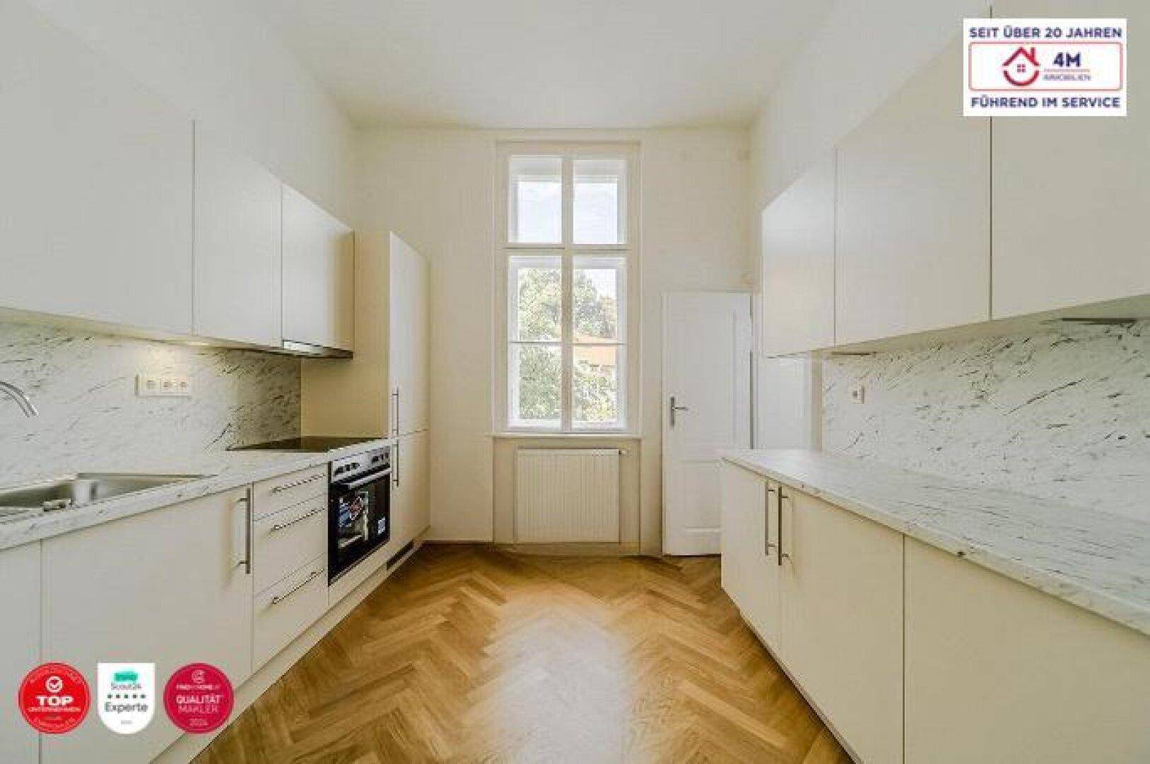Helle Küche mit weißen Schränken, Marmor-Arbeitsplatten und einem Fenster mit Blick ins Grüne.