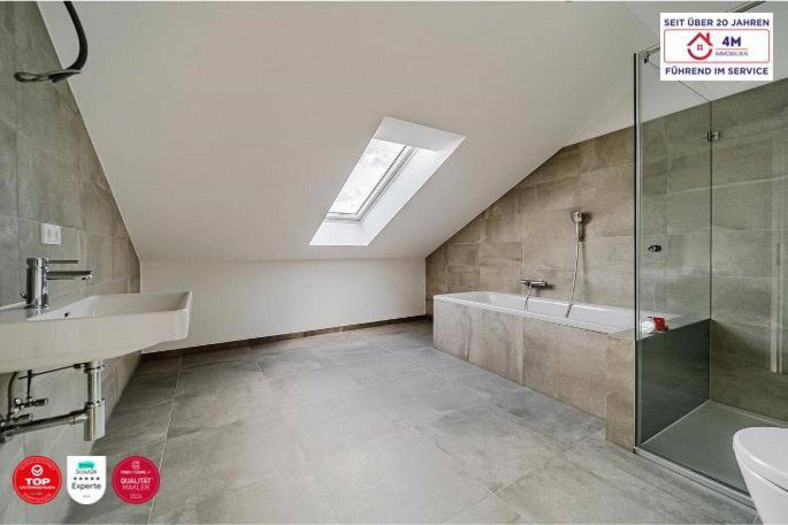 Modernes Dachgeschossbad mit Badewanne, Dusche, Dachfenster und grauen Fliesen.