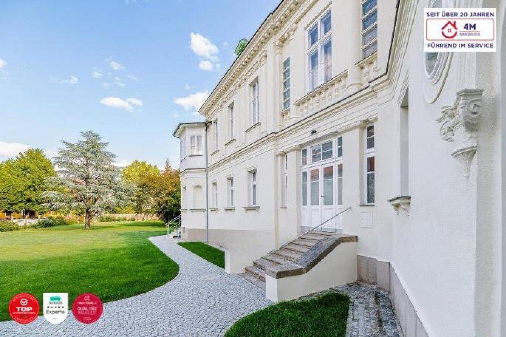 Seitenansicht des klassischen Gebäudes mit weitläufigem Rasen und altem Baumbestand.