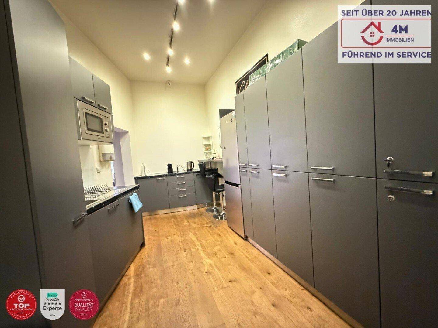 Moderne Küche mit grauen Schränken, Mikrowelle und Holzboden, bietet viel Stauraum und Arbeitsfläche.