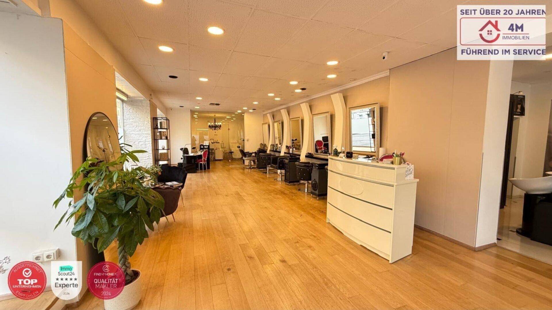Langer Friseursalon mit Holzboden, vielen Spiegeln und Arbeitsplätzen, beleuchtet durch Deckenstrahler und Tageslicht.